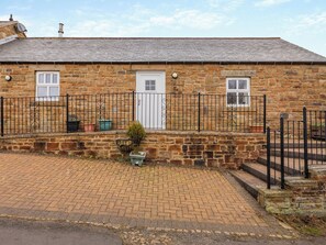A stone building with a brick driveway, a white door, and a black metal fence. - 3 bedroom accommodation in Cowshill, near Alston (Cowshill, near Alston)