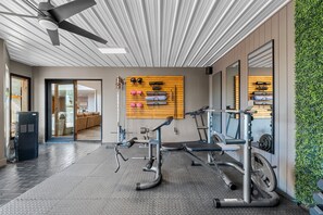 Un gimnasio con equipo de ejercicio, un estante empotrado con pesas y un ventilador de techo.