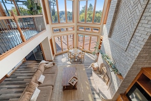 A spacious interior with a high ceiling, a central seating area with a coffee table, and a view through large windows to an outdoor patio.