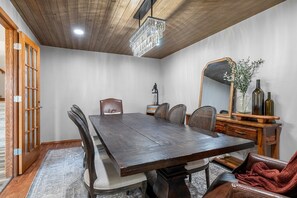 A dining room with a large wooden table, chairs, a chandelier, and a mirror on the wall.