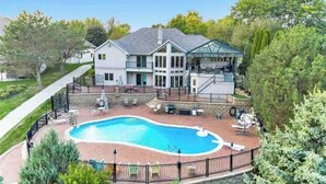 Una casa de dos pisos con piscina, mobiliario exterior y un patio cubierto.