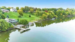 Una propiedad frente al lago con un muelle, una colina cubierta de césped y una casa.