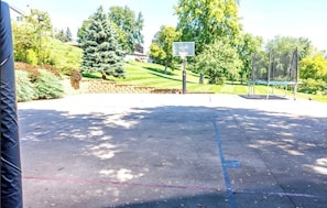 Ein Basketballplatz im Freien mit Korb, umgeben von Bäumen und einer Steinmauer.