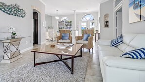 A spacious living room with a white sofa, two wicker armchairs, and a glass coffee table.