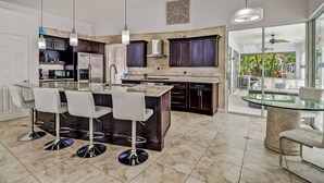 A modern kitchen with dark cabinets, a central island with bar stools, and a glass dining table.
