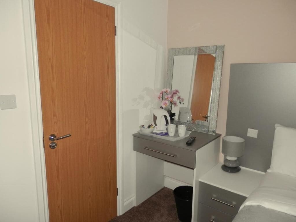 Un dormitorio con puerta de madera, una mesita de noche con lámpara, un espejo y una cama.