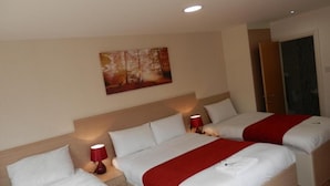 Quarto de hotel com três camas, cada uma com roupa de cama branca e detalhes vermelhos. Há uma pintura na parede acima das camas, e uma porta à direita.