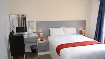 Una habitación de hotel con cama, mesita de noche, lámpara, silla, escritorio y espejo.