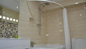 Um banheiro moderno com uma banheira livre, um chuveiro com box de vidro curvo e um vaso sanitário.