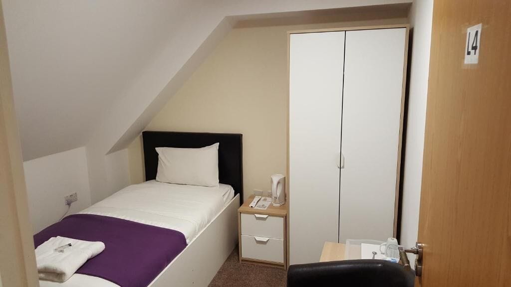 A small, neatly arranged bedroom with a bed, a nightstand, a wardrobe, and a chair.