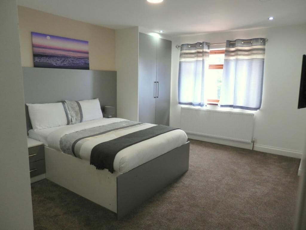Un dormitorio con cama, mesita de noche, armario y ventana con cortinas.