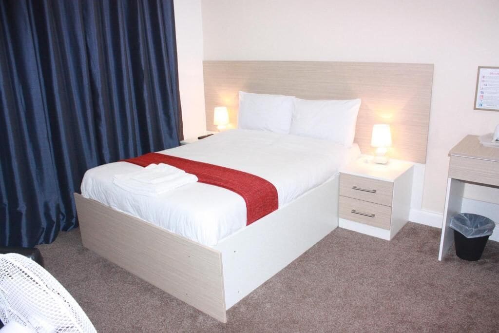 A hotel room with a bed, bedside lamps, a desk, and a trash bin.