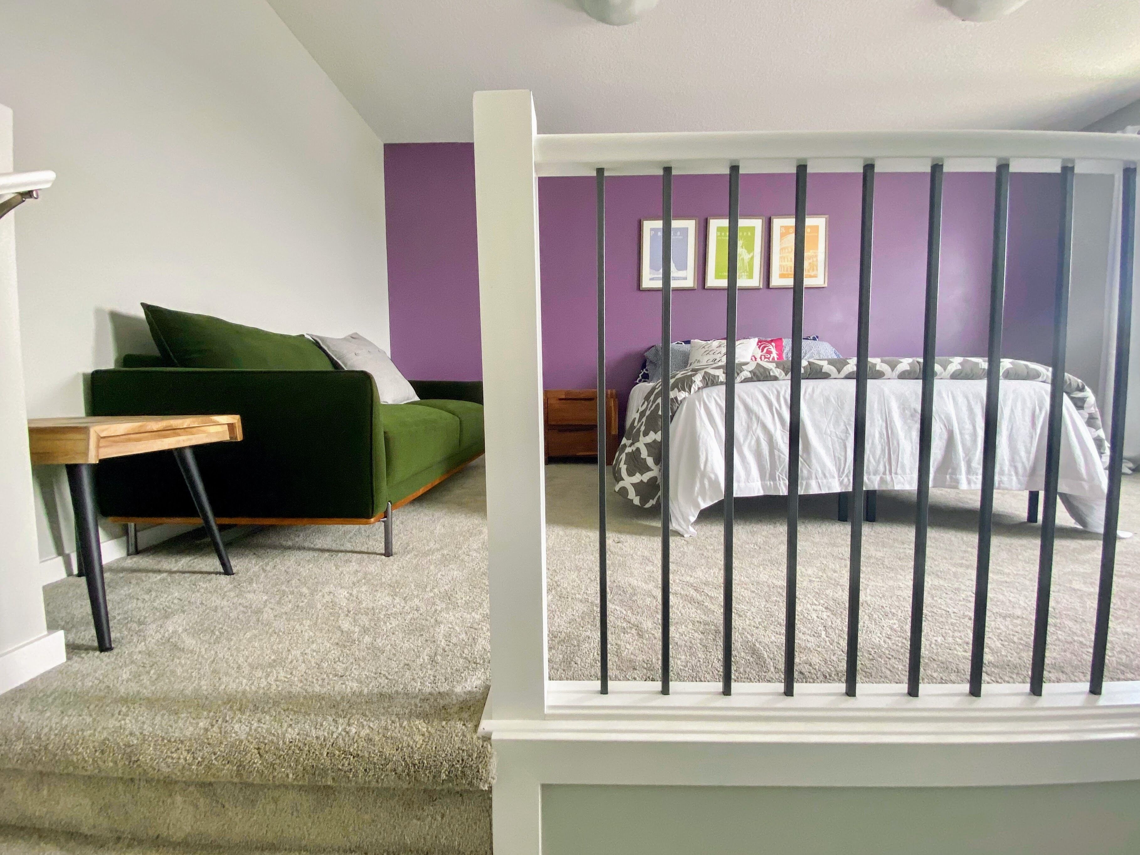 Een slaapkamer met een groene bank, een bed met beddengoed met een patroon, en een trap met een leuning.