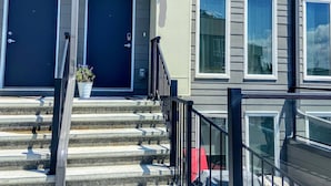 A row of townhouses with a central staircase leading to the entrance, a small outdoor area with steps, and a metal railing. - 3 bedroom Townhouse Rooftop Patio & AC (Calgary)