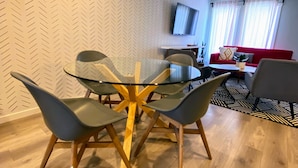 A modern dining area with a glass table and four chairs, a red sofa, and a TV mounted on the wall. - 3 bedroom Townhouse Rooftop Patio & AC (Calgary)