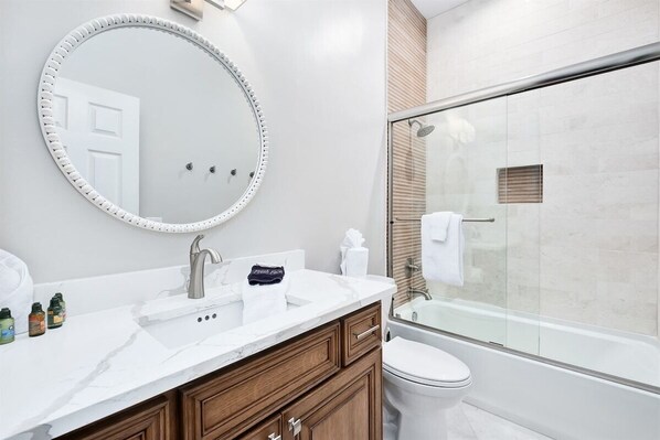 A modern bathroom with a round mirror, a sink, a toilet, and a glass-enclosed shower.