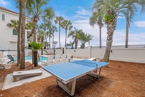 Una mesa de ping pong al aire libre rodeada de palmeras y una piscina.