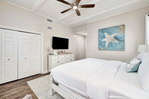 Un dormitorio con cama, ventilador de techo, televisión, cómoda y un cuadro de una estrella de mar en la pared.