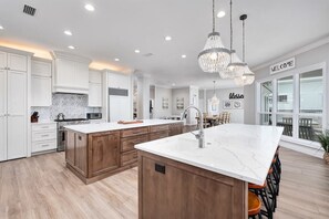 A modern kitchen with white cabinetry, a large island with a sink, and pendant lighting.
