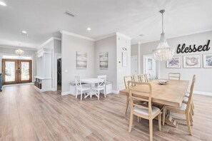 A spacious dining area with a wooden table and chairs, a chandelier, and artwork on the walls.