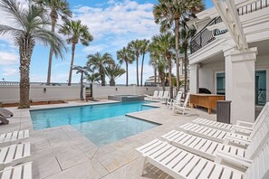 A swimming pool with lounge chairs, palm trees, and a bar area.