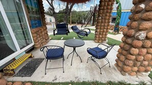 Un patio al aire libre con un columpio, una mesa redonda y cuatro sillas.