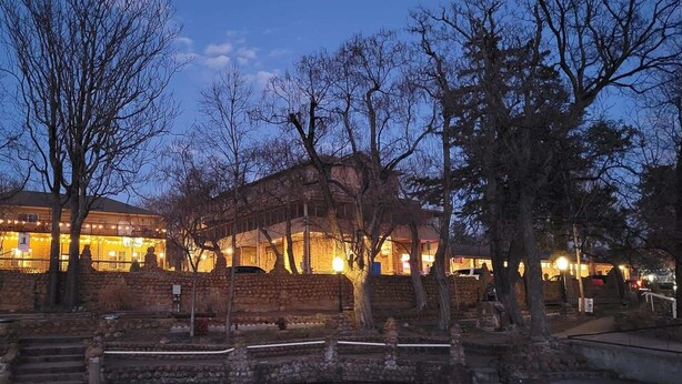 Un edificio storico con pareti in pietra e un porticato, circondato da alberi spogli e un muro di pietra.