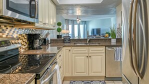 A modern kitchen with a stainless steel refrigerator, a built-in oven, and a microwave. There is a sink with a faucet, and a countertop with a coffee maker and a small plant. - Island House C219 (St. Augustine)