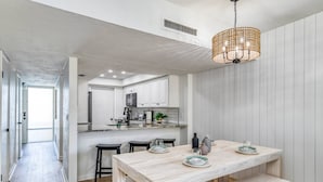 A modern kitchen with white cabinets, a wooden dining table, and a hanging light fixture. - Island House C219 (St. Augustine)
