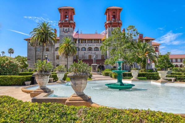 Un edificio histórico con dos torres, una fuente y jardines bien cuidados.
