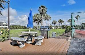 Relax on the patio with a barbecue grill, stone benches, and a round table under a shaded area.