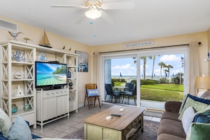 Relax in this inviting living room with a TV, sofa, and coffee table, offering a comfortable space for relaxation or socializing with a view of the golf course and palm trees.
