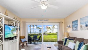A living room with a television, a couch, a coffee table, and a view of the beach. - Sandpiper 113 - Ground Floor Oceanfront (St. Augustine)