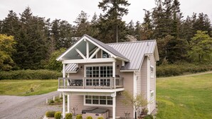 Une maison à deux étages avec un balcon, des fondations en pierre et une cour gazonnée.