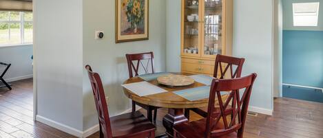 Un comedor con una mesa redonda de madera, cuatro sillas de madera, un mueble de madera con puertas de cristal y un cuadro enmarcado en la pared.