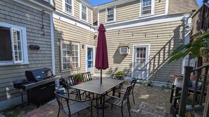 A patio with a table and chairs, a grill, and a red umbrella. - 4 BR Antique Provincetown Single Family Home in the Center of Town - Sleeps 9! (Provincetown)
