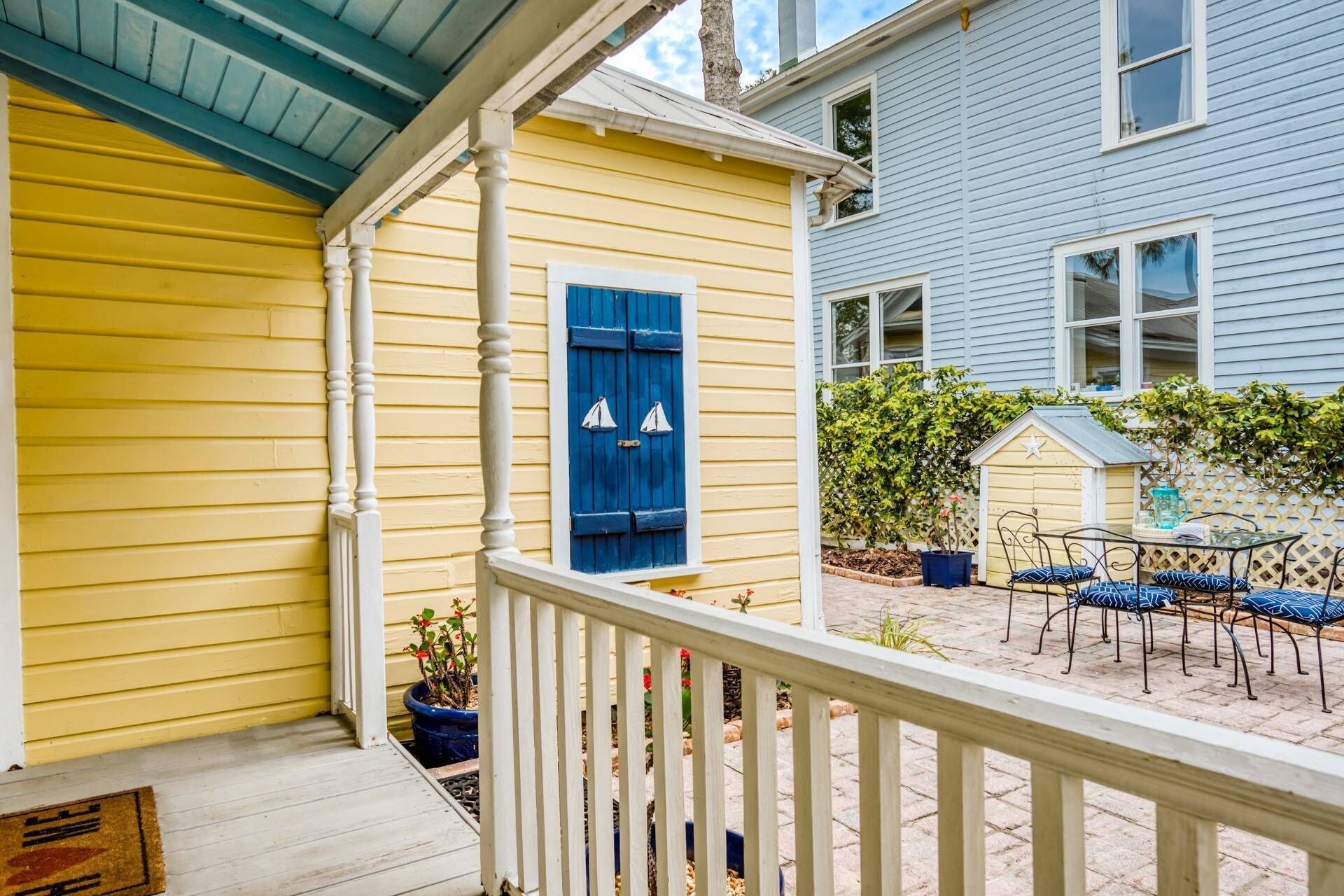 A yellow house with a blue window and a small deck with chairs and a table.