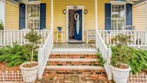A yellow house with a porch, a blue door, and a brick staircase. - Little Yellow Cottage on Water Street (St. Augustine)