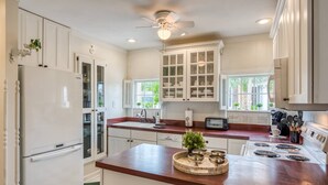 A kitchen with white cabinets, a wooden countertop, a built-in stove, and a ceiling fan. - Little Yellow Cottage on Water Street (St. Augustine)