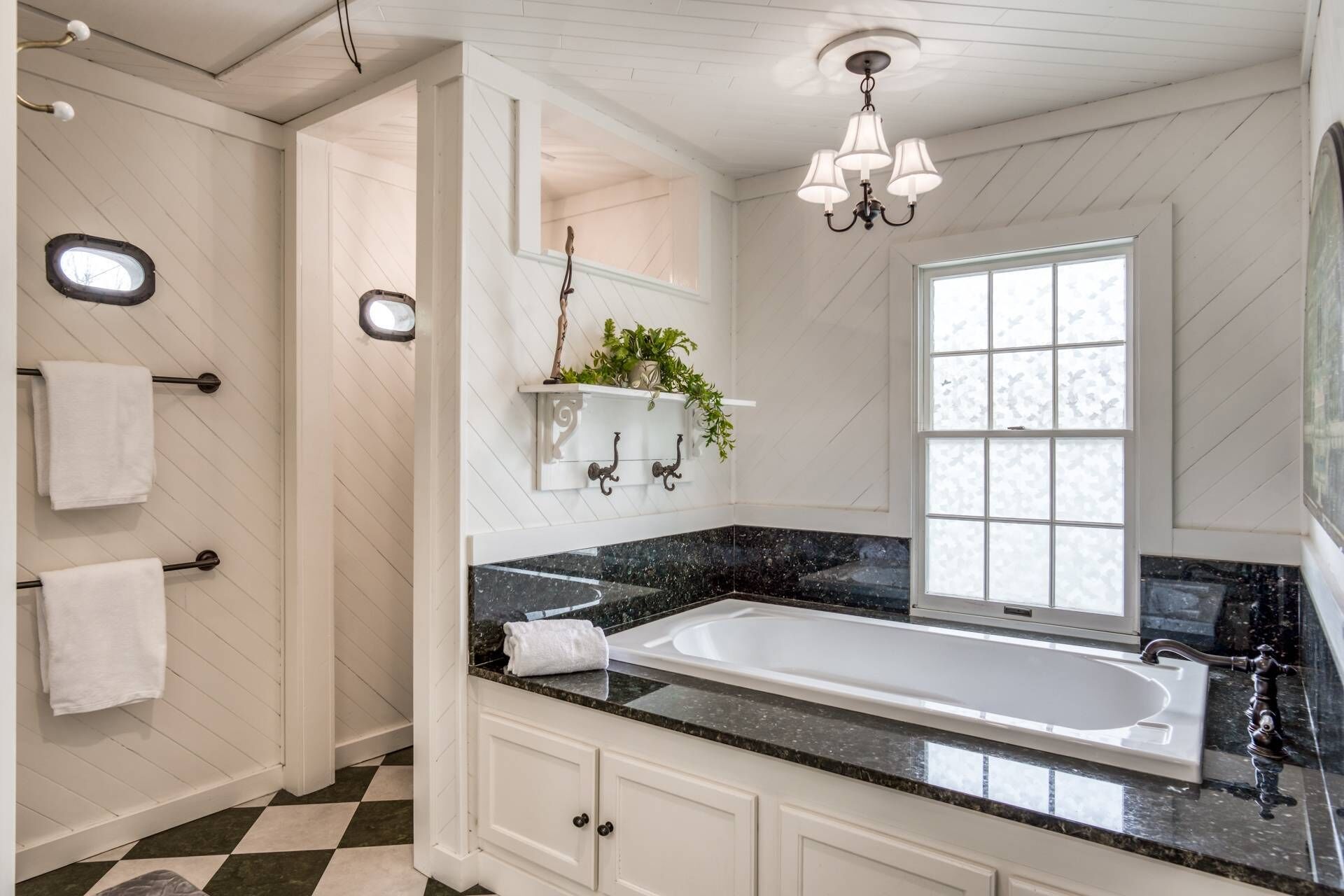 A bathroom with a black marble sink, white cabinets, a large mirror, and a window with frosted glass.