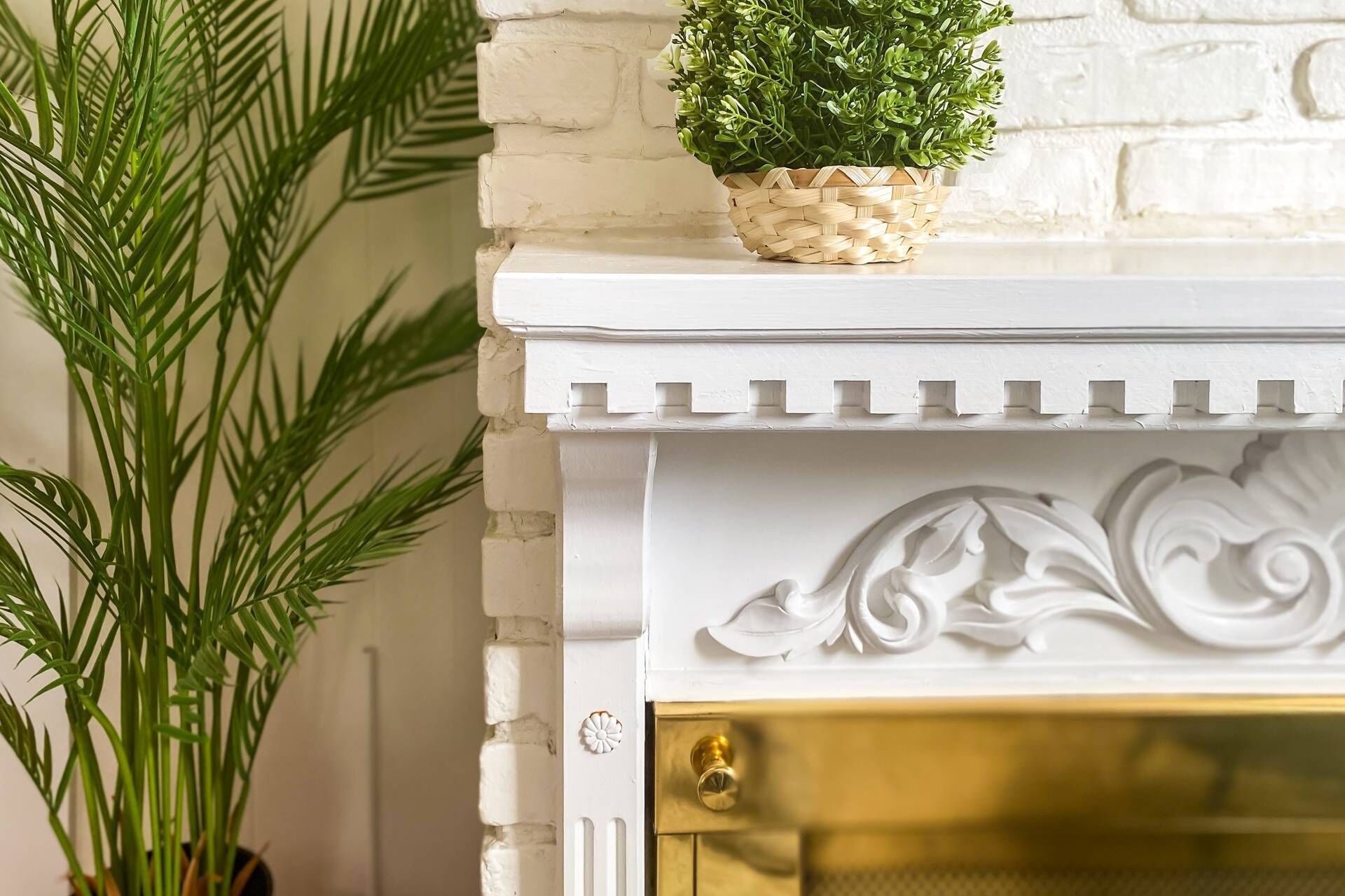 Een wit metselwerk schouw met een decoratieve witte plint en een deur in goudkleur.
