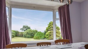 Une salle à manger avec une table dressée pour quatre personnes, de grandes fenêtres avec des rideaux et une vue sur un jardin.
