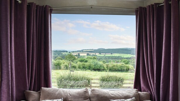 Une pièce avec une grande fenêtre, un canapé beige et des rideaux violets.