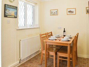 Un comedor con mesa de madera dispuesta para cuatro personas, ventana con vistas y un cartel en la pared.