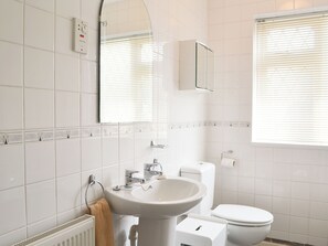 Un baño moderno con azulejos blancos, un lavamanos, un inodoro, un espejo y una ventana con persianas.