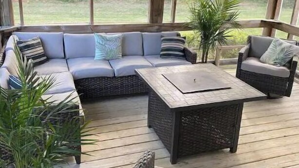 Uma área de estar coberta ao ar livre, com um sofá, cadeiras e uma mesa.