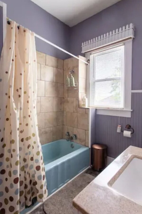 A bathroom with a bathtub, a shower area, and a window.