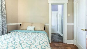 A bedroom with a bed, a door, and a hallway leading to another room.