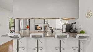 A modern kitchen with a central island, bar stools, stainless steel appliances, and a small potted plant. - Magnolia House w/ 4 Beds 2 Baths on 1.5 Acres ⭐ (Magnolia)