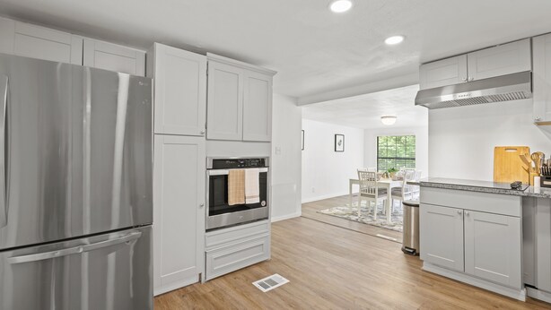 A modern kitchen with stainless steel appliances, white cabinetry, and a dining area with a wooden table and chairs. - Magnolia House w/ 4 Beds 2 Baths on 1.5 Acres ⭐ (Magnolia)